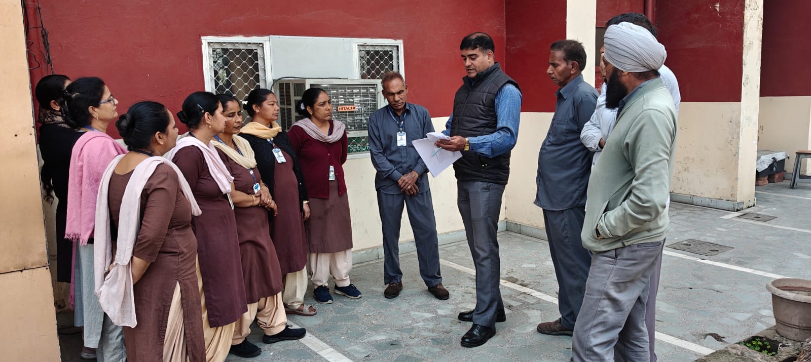 A group of school staff listening to a speaker during an outdoor briefing